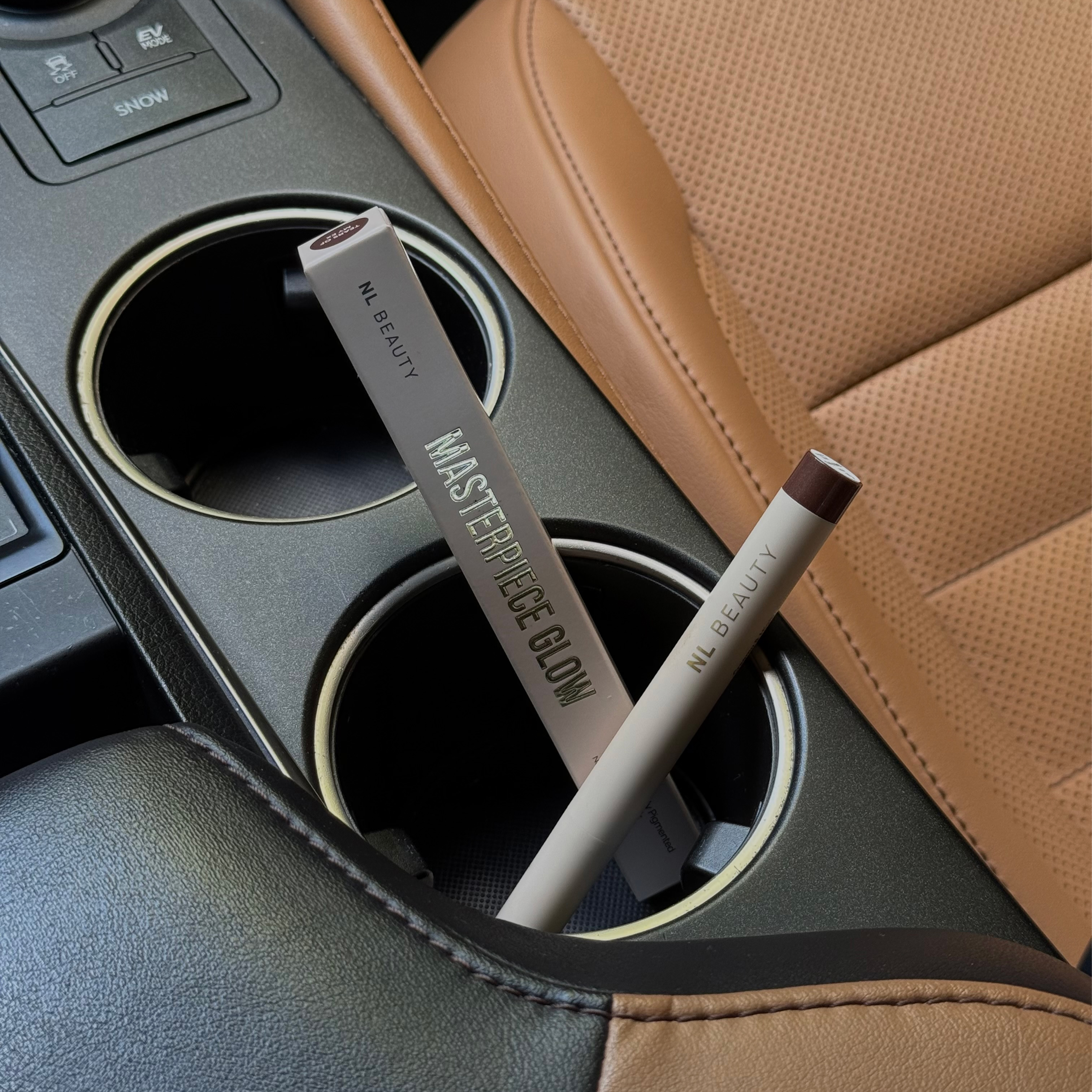 Two NL Beauty makeup products rest inside the cup holders of a car's center console.
