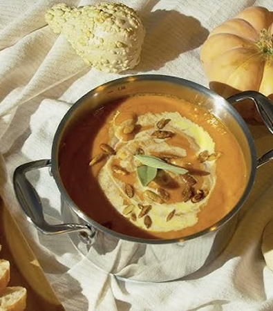 Creamy pumpkin soup in a pot, garnished with seeds and sage leaves.