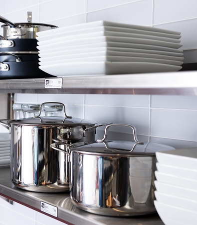 Metal pots and white plates neatly arranged on industrial kitchen shelves.