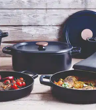 Black cookware set with food, placed on a wooden surface.