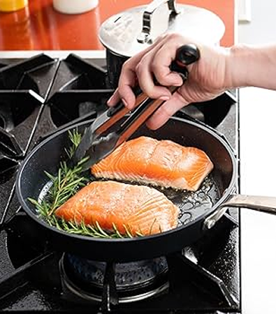 Salmon fillets being pan-seared with rosemary in a non-stick skillet.