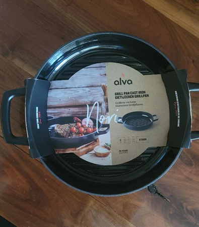Cast iron grill pan with two handles and packaging label on a wooden surface.