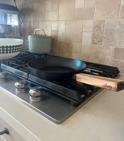 A frying pan with a wooden handle on a stovetop next to a pot and bowl.
