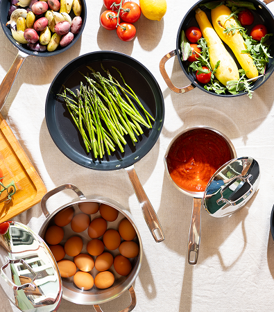 Array of colorful vegetables and eggs in cookware on a light tablecloth.