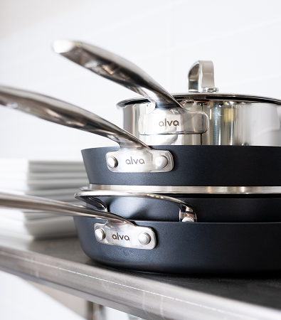 A stack of shiny, metal and non-stick Alva cookware on a kitchen counter.