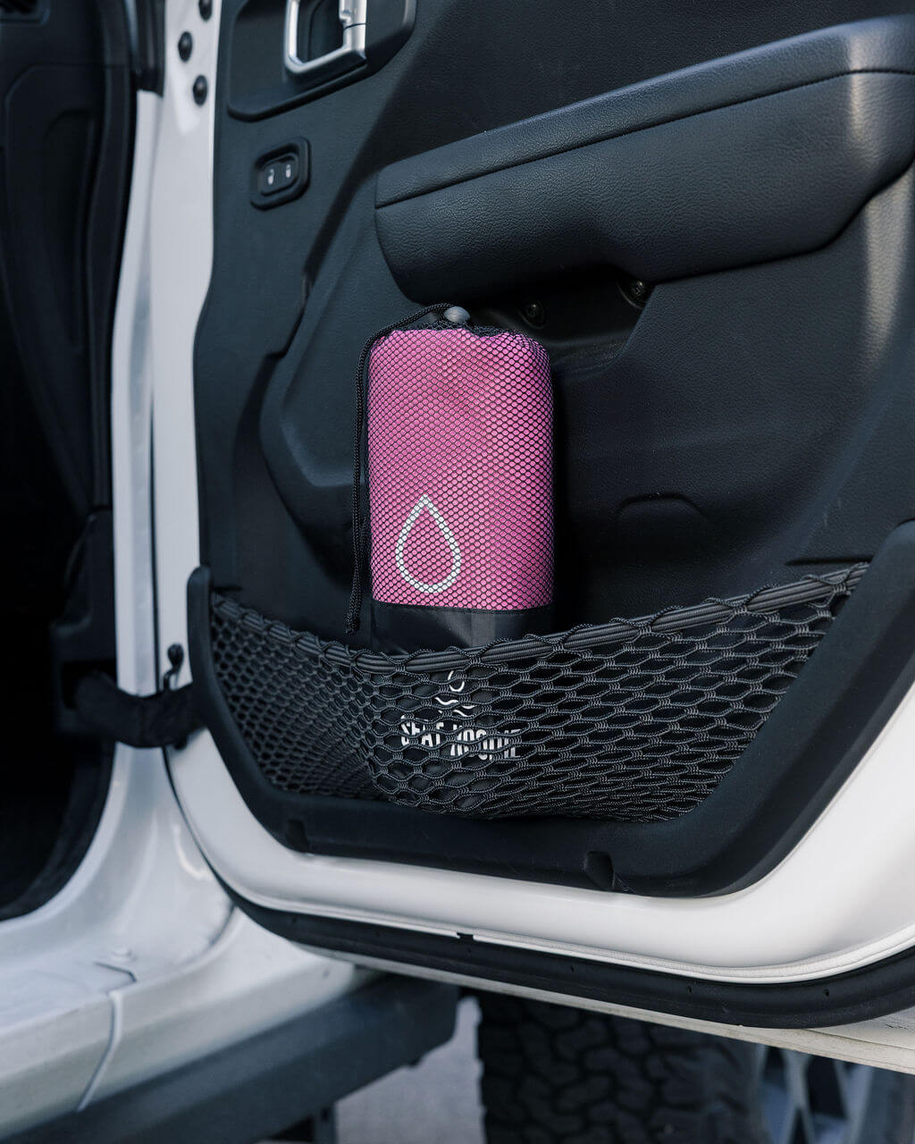A pink mesh bag with a teardrop logo sits in a car door's mesh storage pocket.