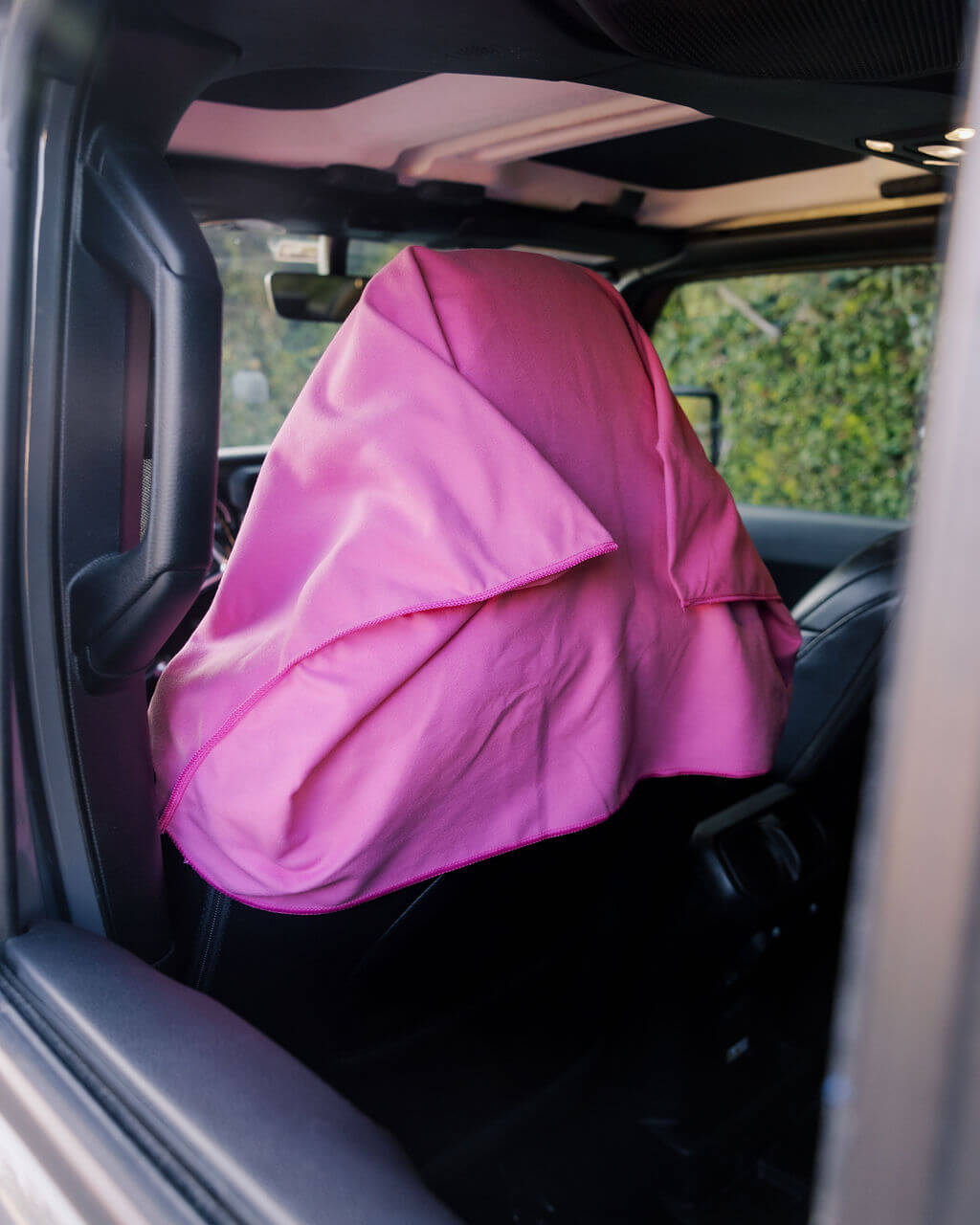 A bright pink cloth is draped over the headrest of a car seat.