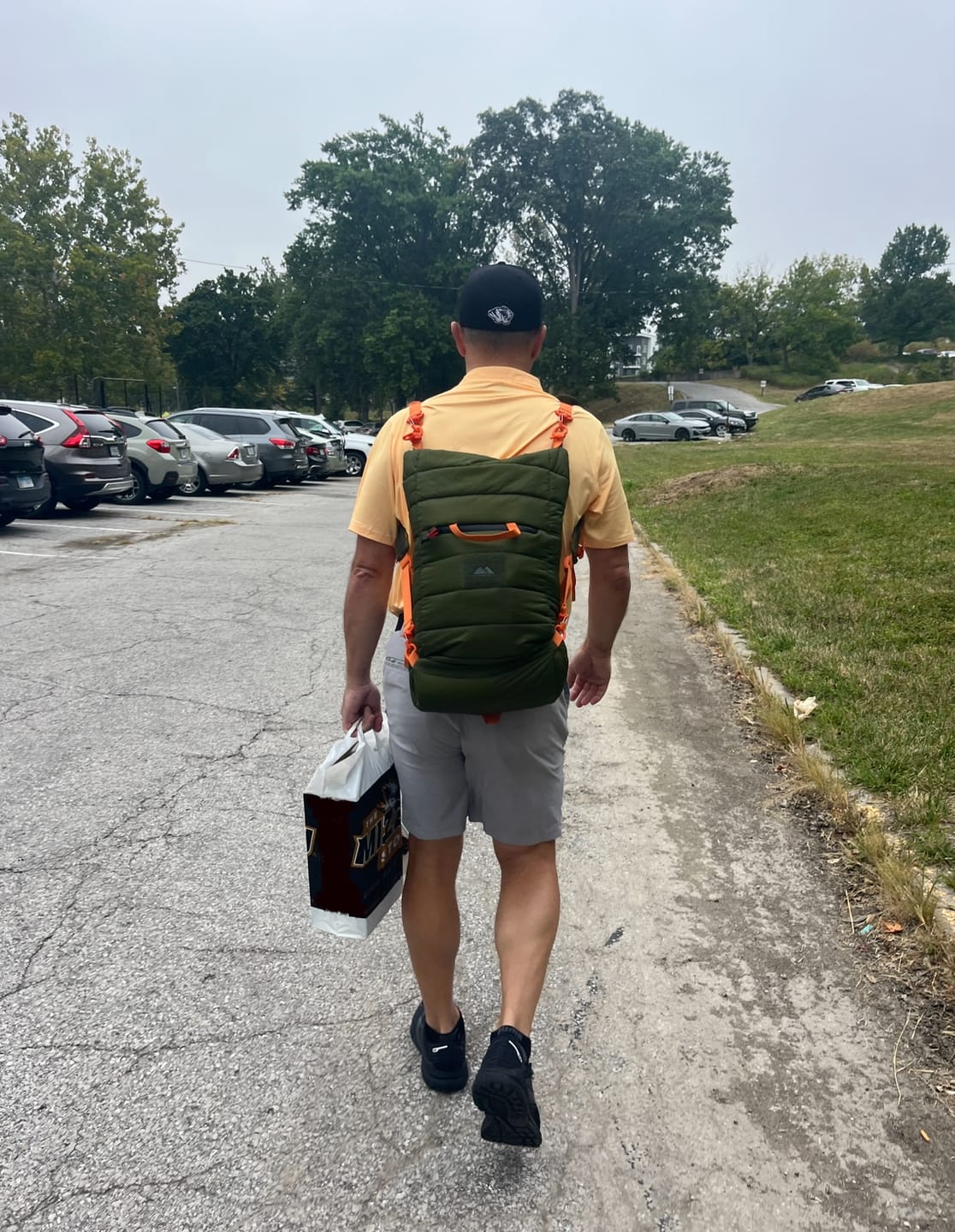 Person walking in a parking lot with a backpack and a shopping bag.