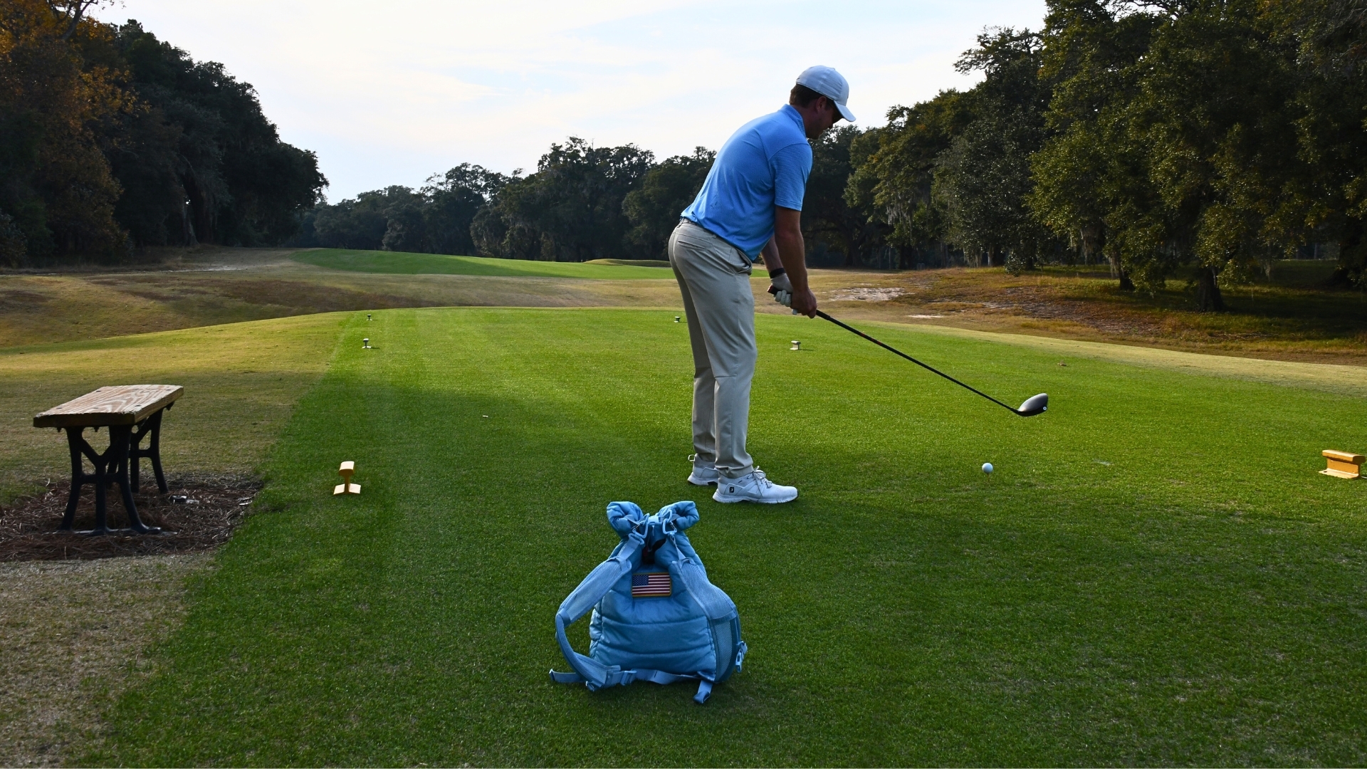 Person preparing to tee off on a golf course with a backpack nearby.