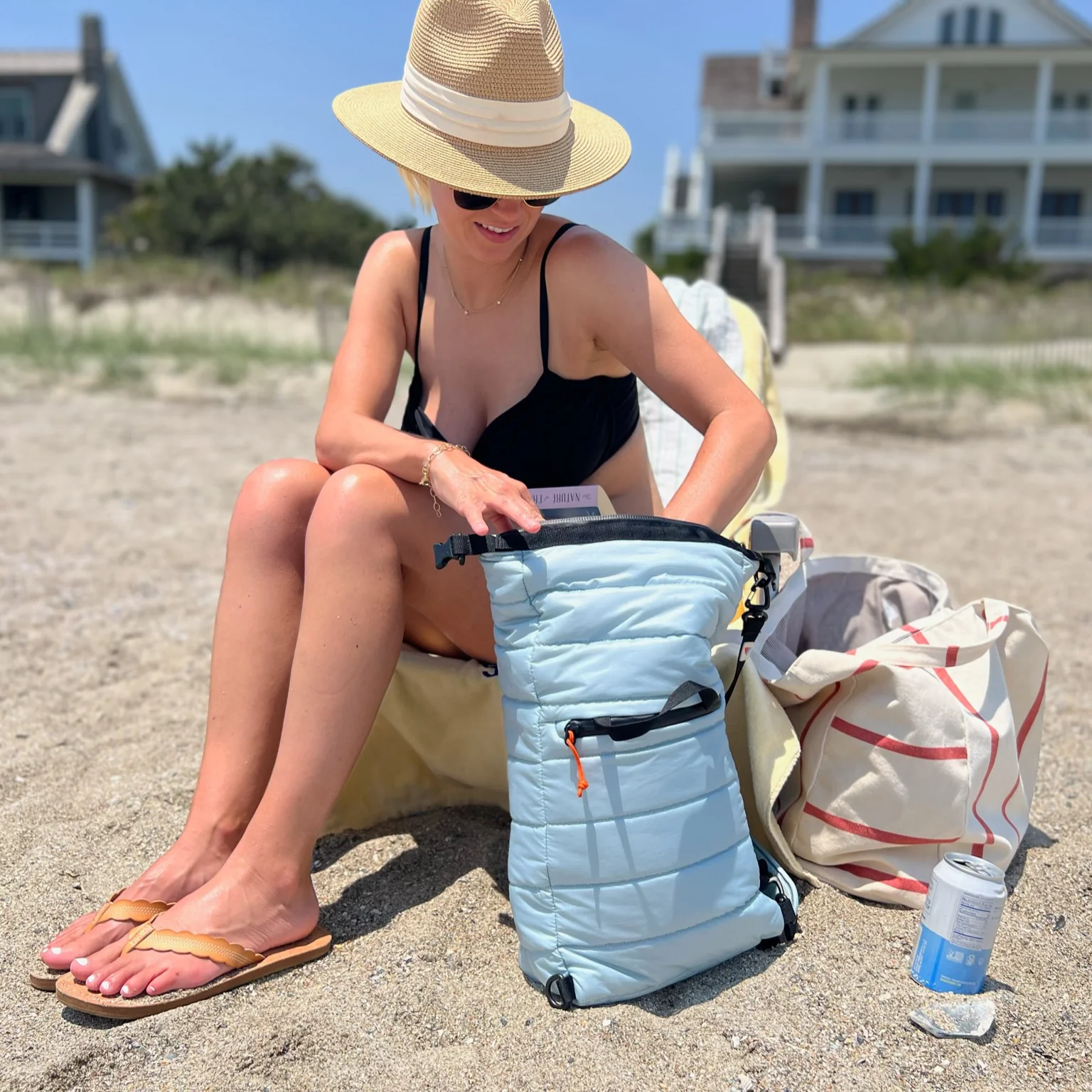 Person in swimsuit and sunhat at the beach, checking a light blue backpack.