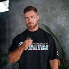 A man with short brown hair and a beard, wearing a black t-shirt, holds a small object.