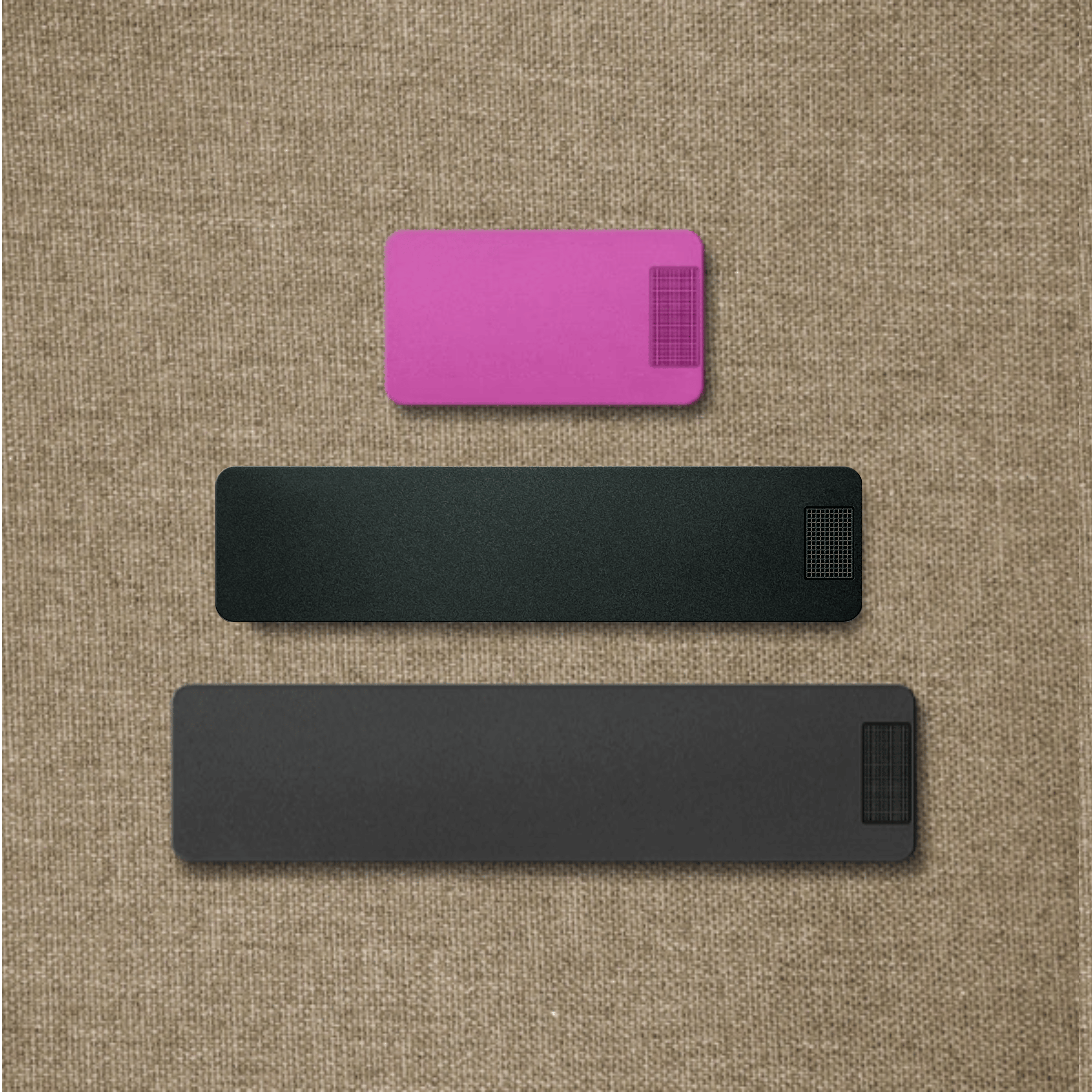 Three rectangular objects in pink and two shades of gray on a brown woven surface.