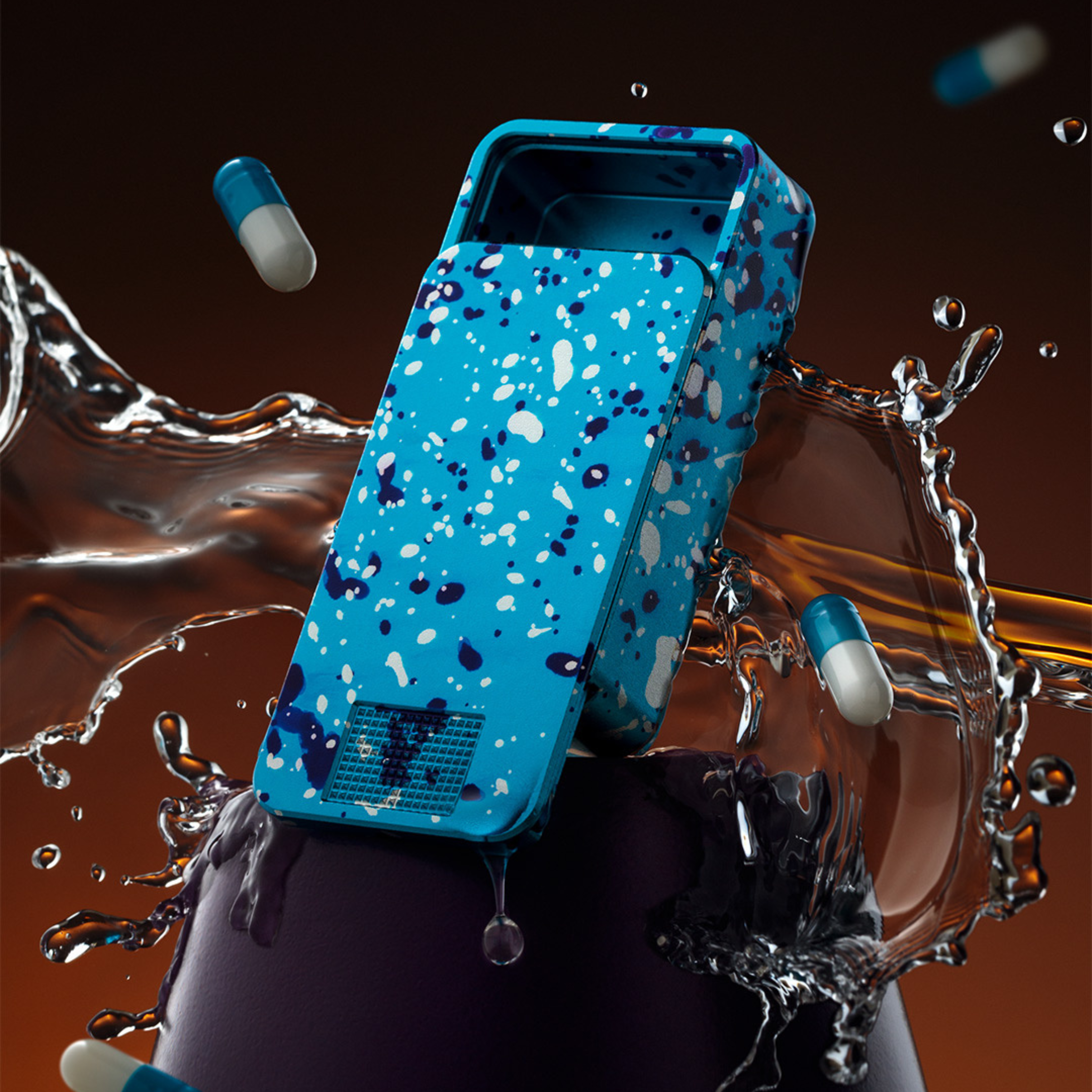 An open, blue paint-splattered case sits in a dynamic splash of liquid with several blue and white capsules floating.