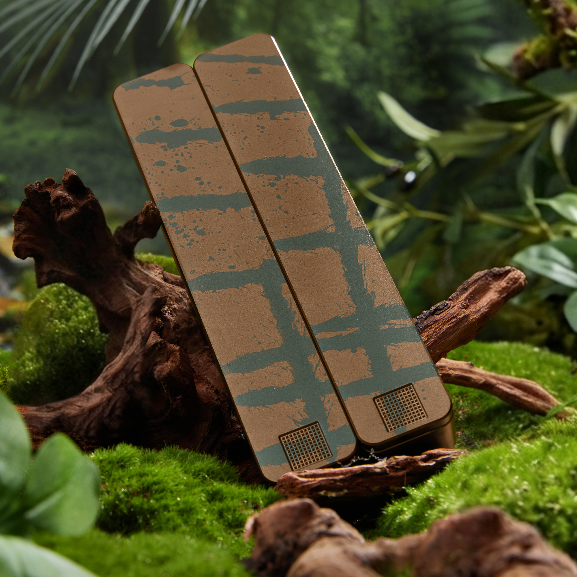 Two brown and green patterned devices resting on moss and driftwood in a jungle-like setting.