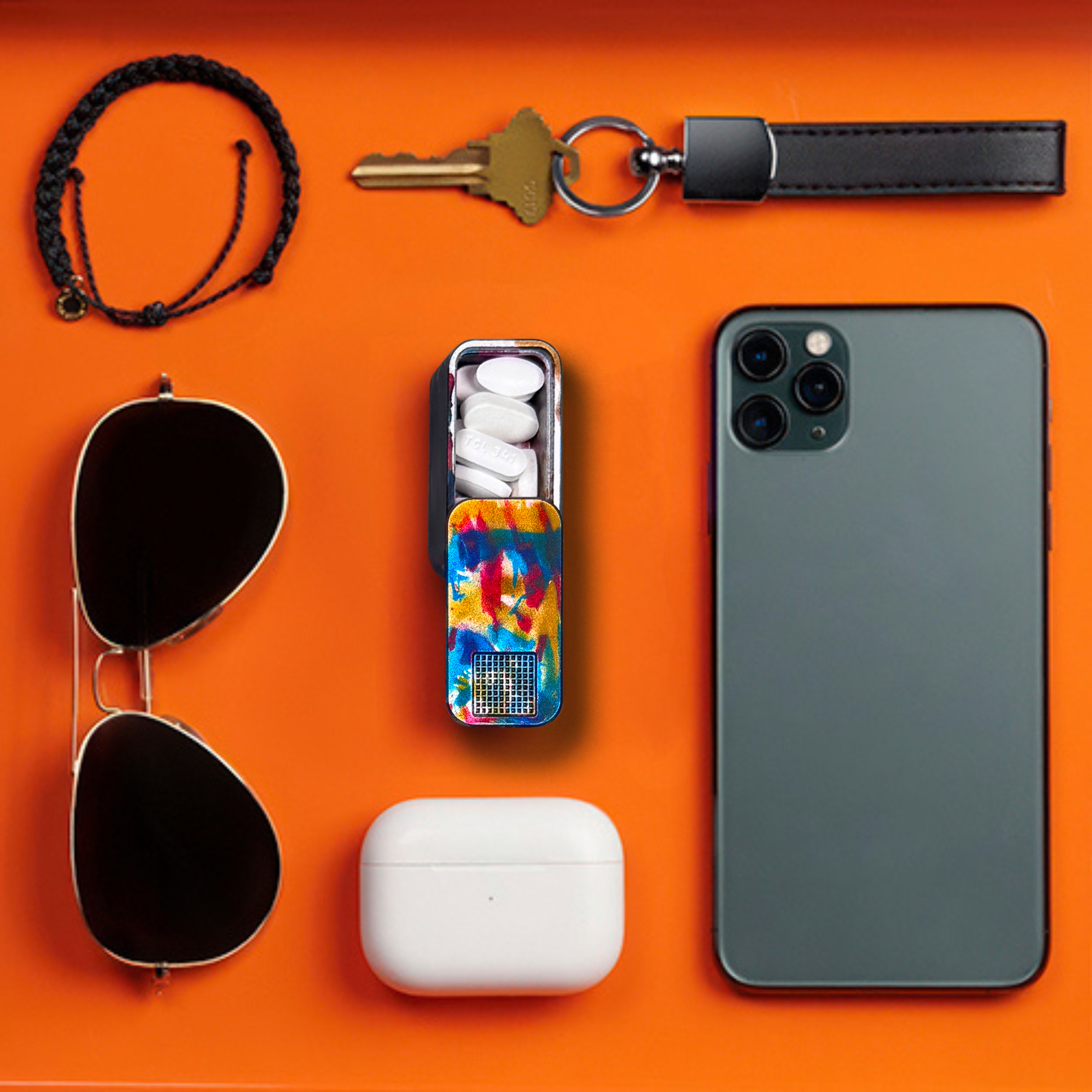 Sunglasses, bracelet, phone, keychain, pill case, earbuds on orange background.