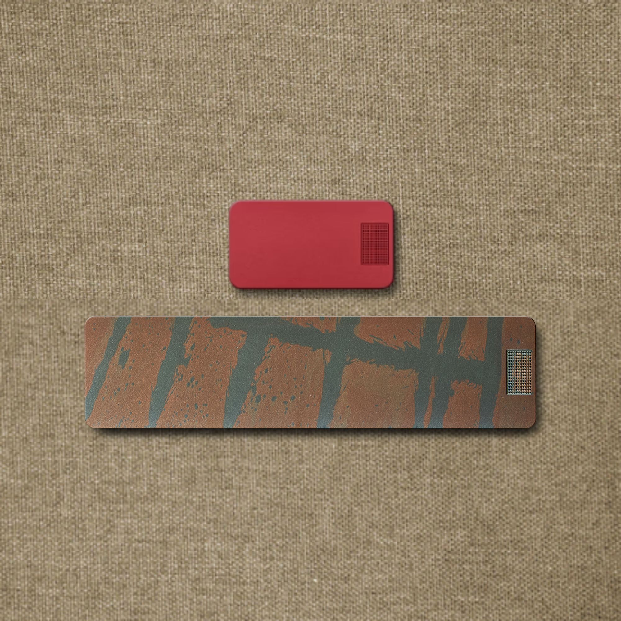 A small red rectangle and a larger, patterned rectangle arranged on a textured, light brown fabric.