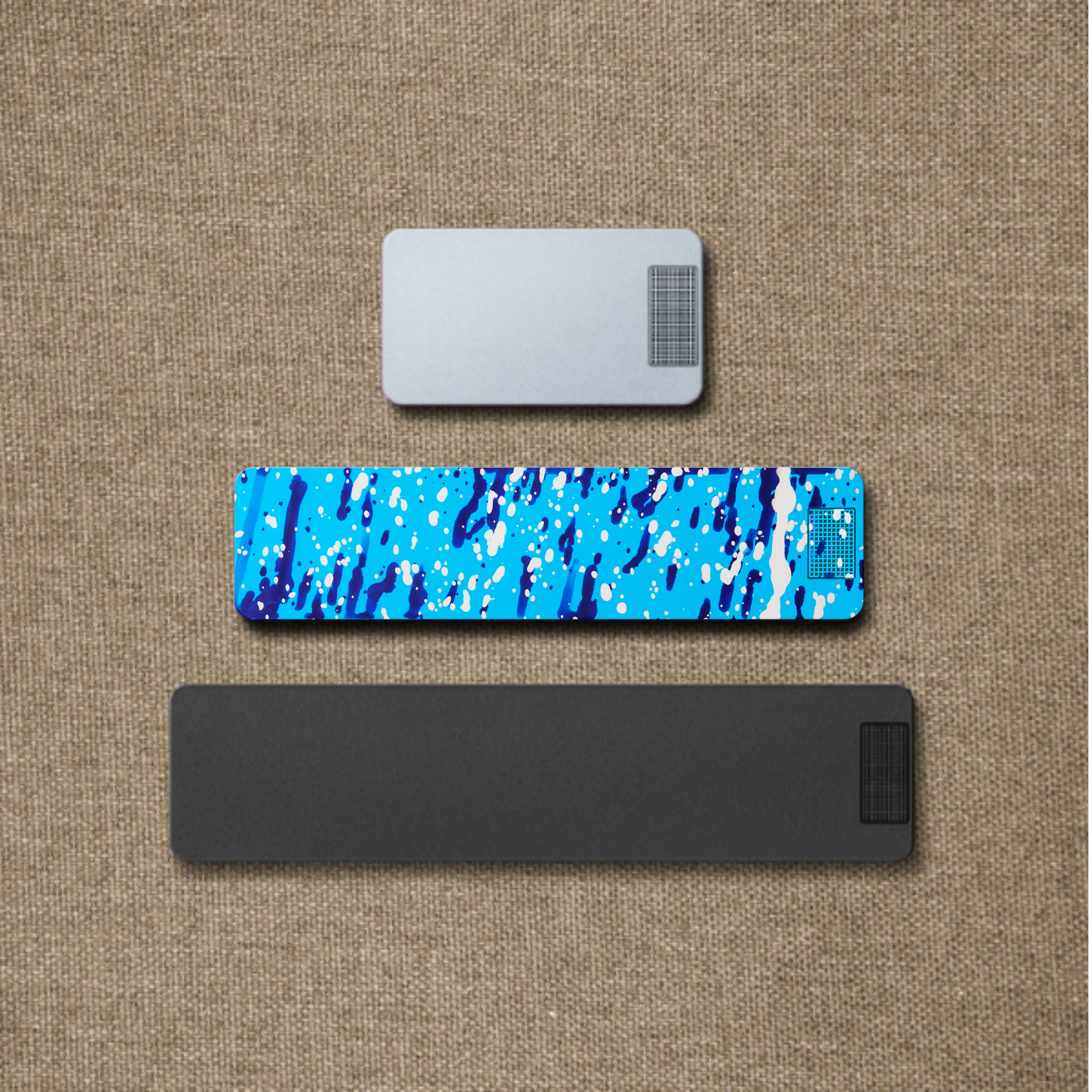 Three rectangular objects in silver, blue splatter print, and black on a textured burlap background.
