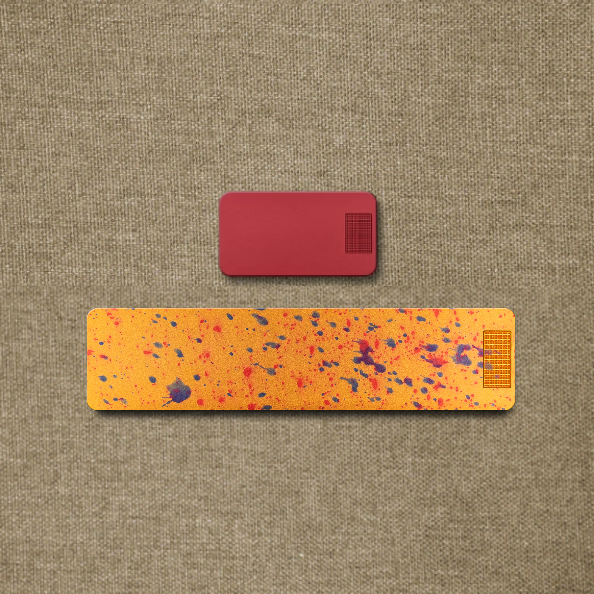 A small red rectangle placed above a longer, paint-splattered orange rectangle on a textured brown surface.