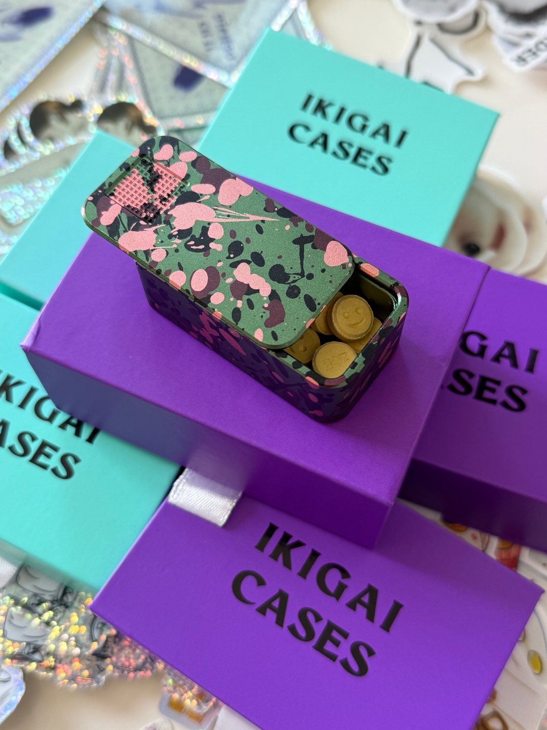 A decorative tin of smiley-face pills sits atop purple and teal 'IKIGAI CASES' boxes.