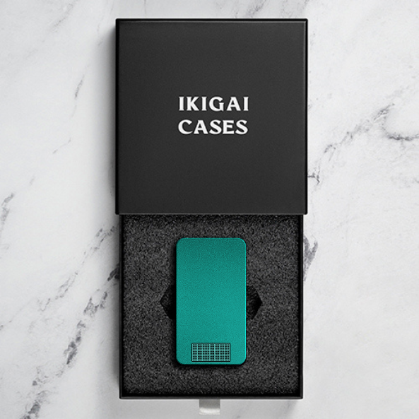 Teal phone case in an open black box with 'IKIGAI CASES' text.