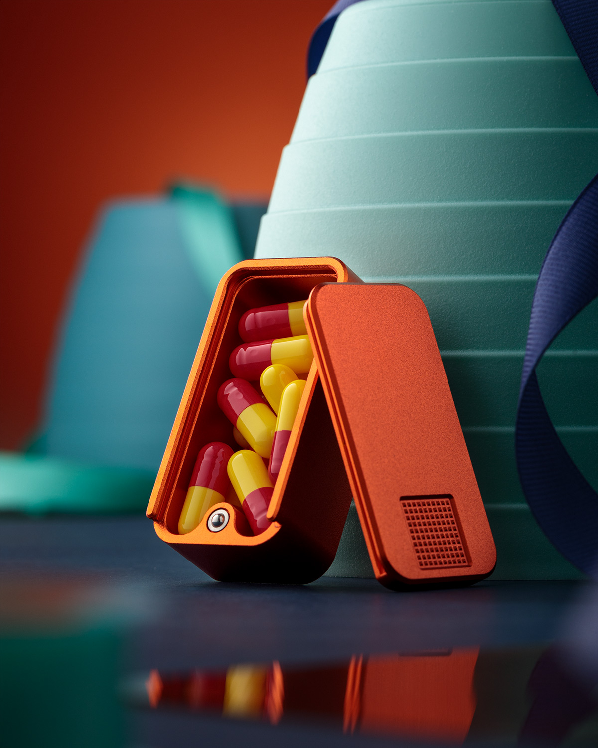 An open, orange triangular container filled with red and yellow capsules sits on a reflective surface.