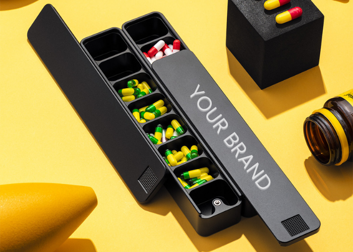 An open black weekly pill organizer with the text 'YOUR LOGO / BRAND HERE' on the lid.