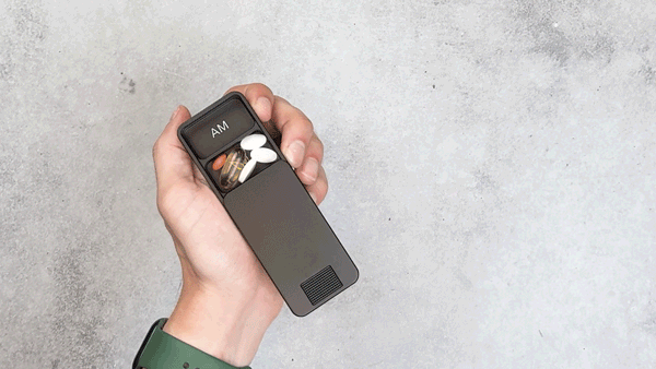 Hand holding a pill organizer with visible compartments labeled 'AM'.