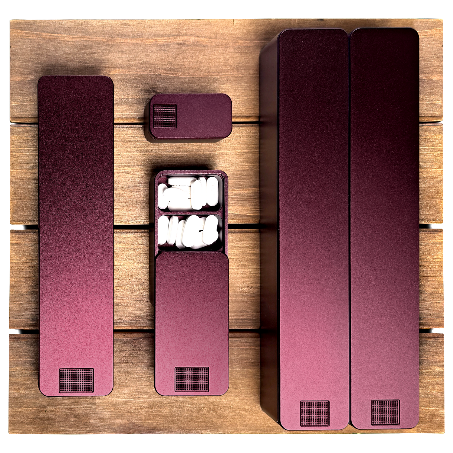 A top-down view of several maroon pill organizers on a wooden surface, one open with white pills.