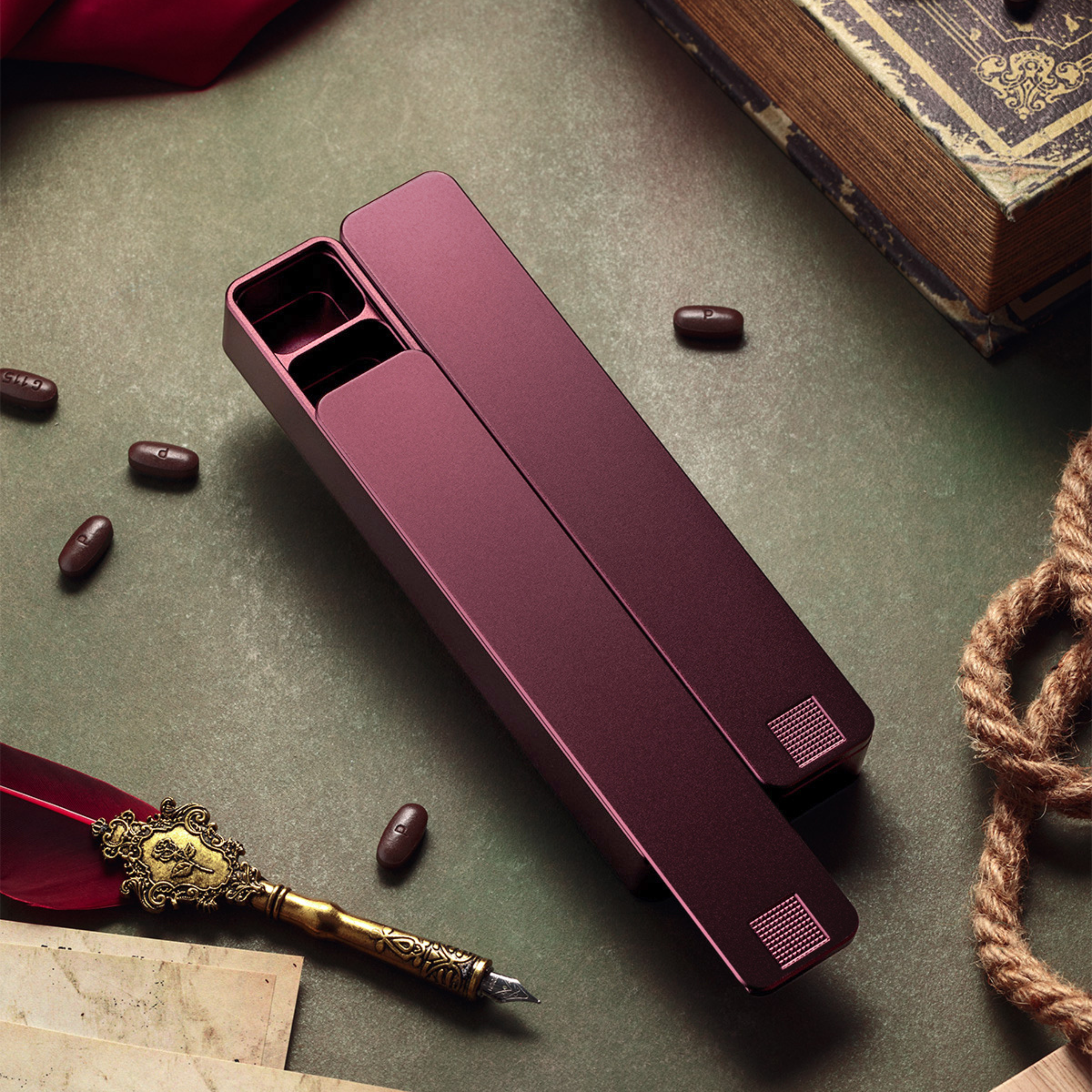An open maroon pill case on a desk with scattered pills, an old book, and a quill pen.