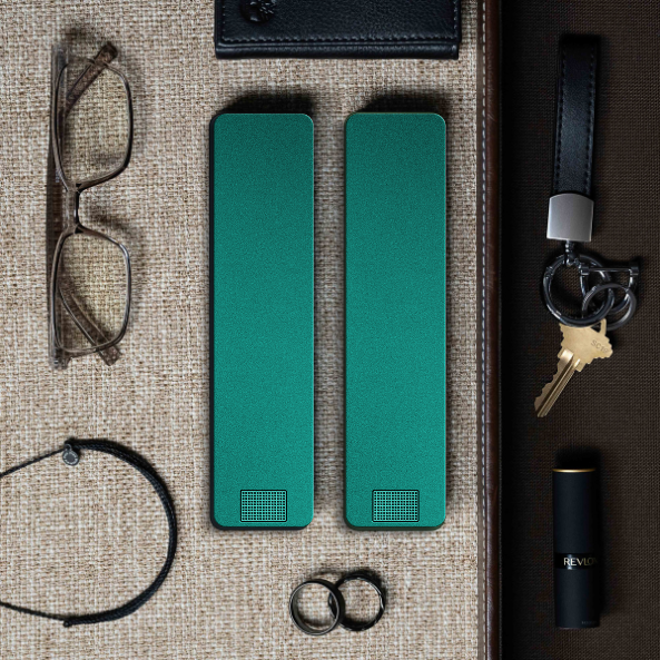 Glasses, green objects, wallet, keys, rings, bracelet, and lipstick arranged on textured background.
