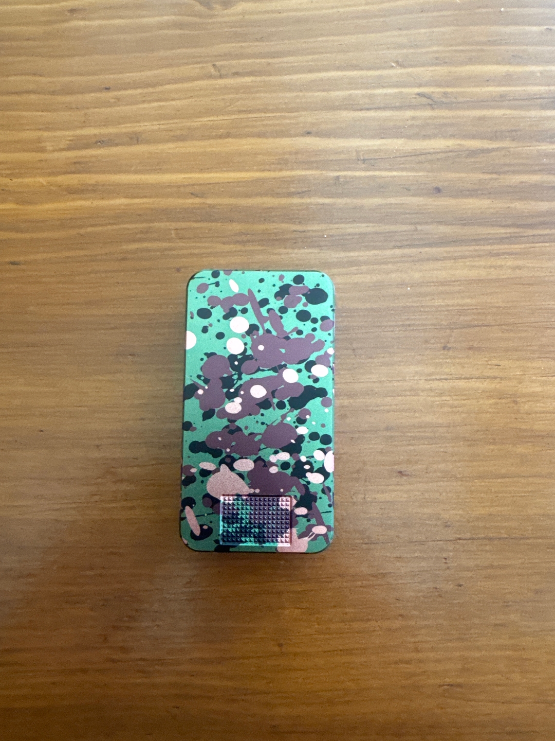 A rectangular device with a green, brown, and white paint splatter design on a wooden table.