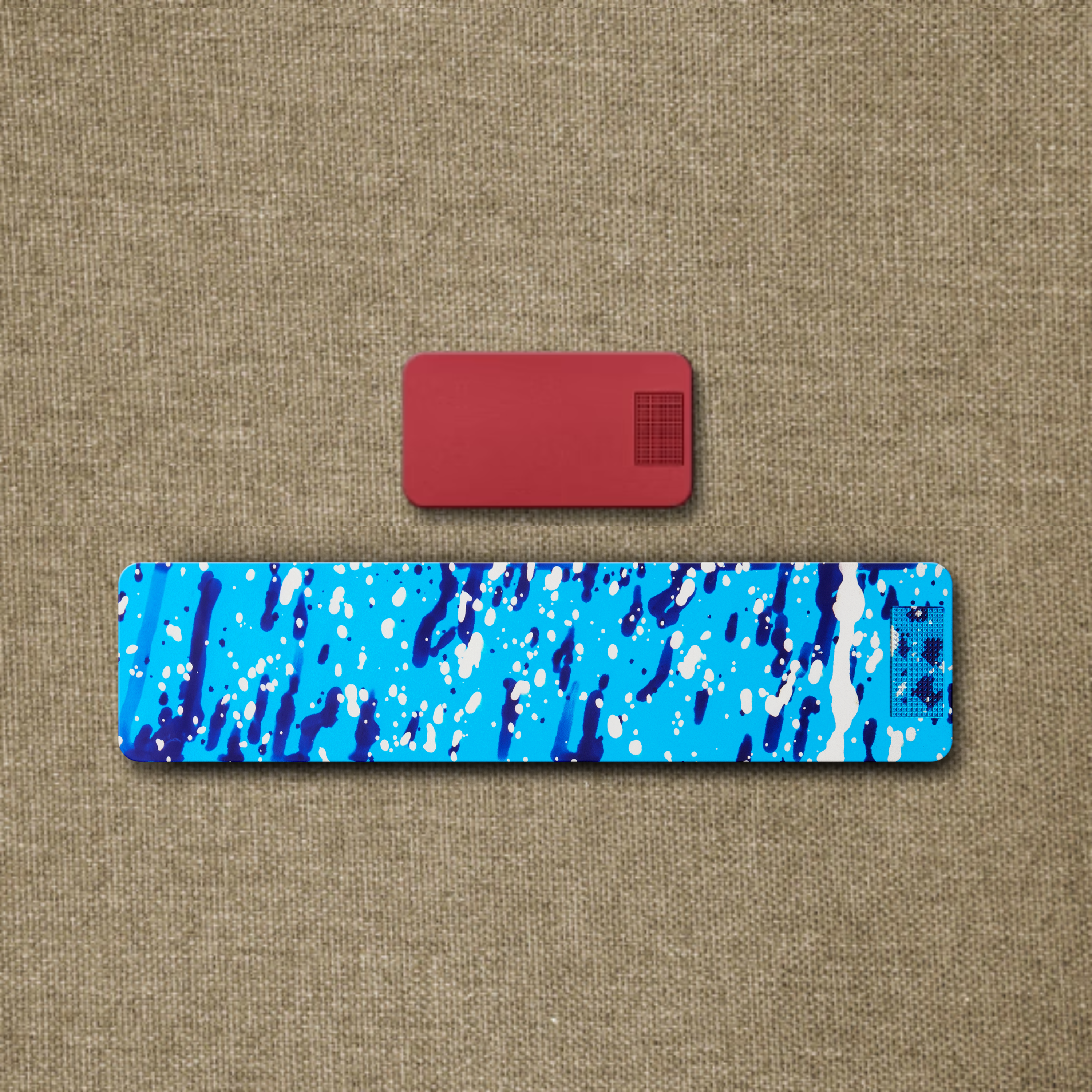 A small red wrist rest and a larger blue and white paint-splattered wrist rest on a textured background.