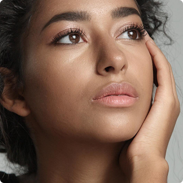 A close-up of a woman with brown eyes looking up, her hand gently touching her cheek.