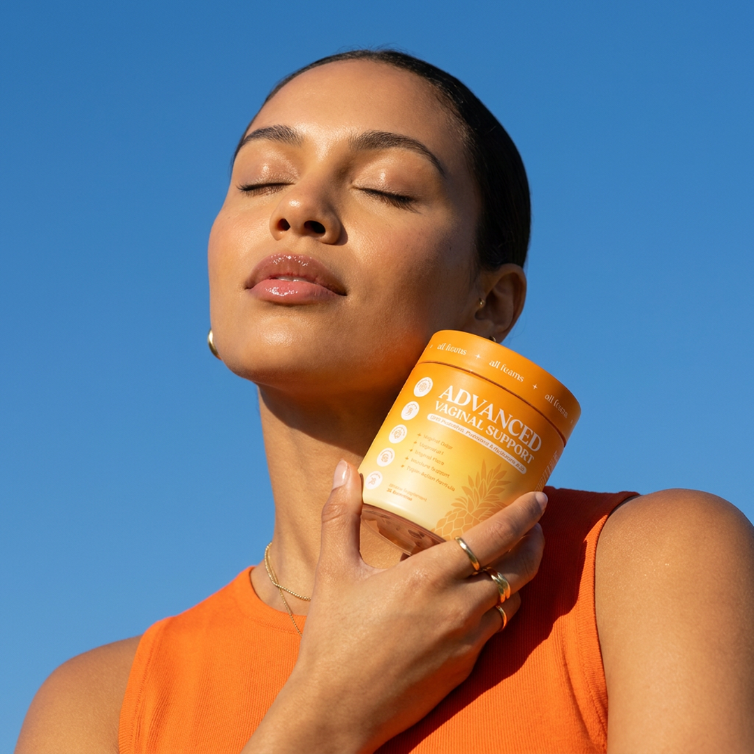 A woman with her eyes closed holds a bottle of Advanced Vaginal Support against a clear blue sky.