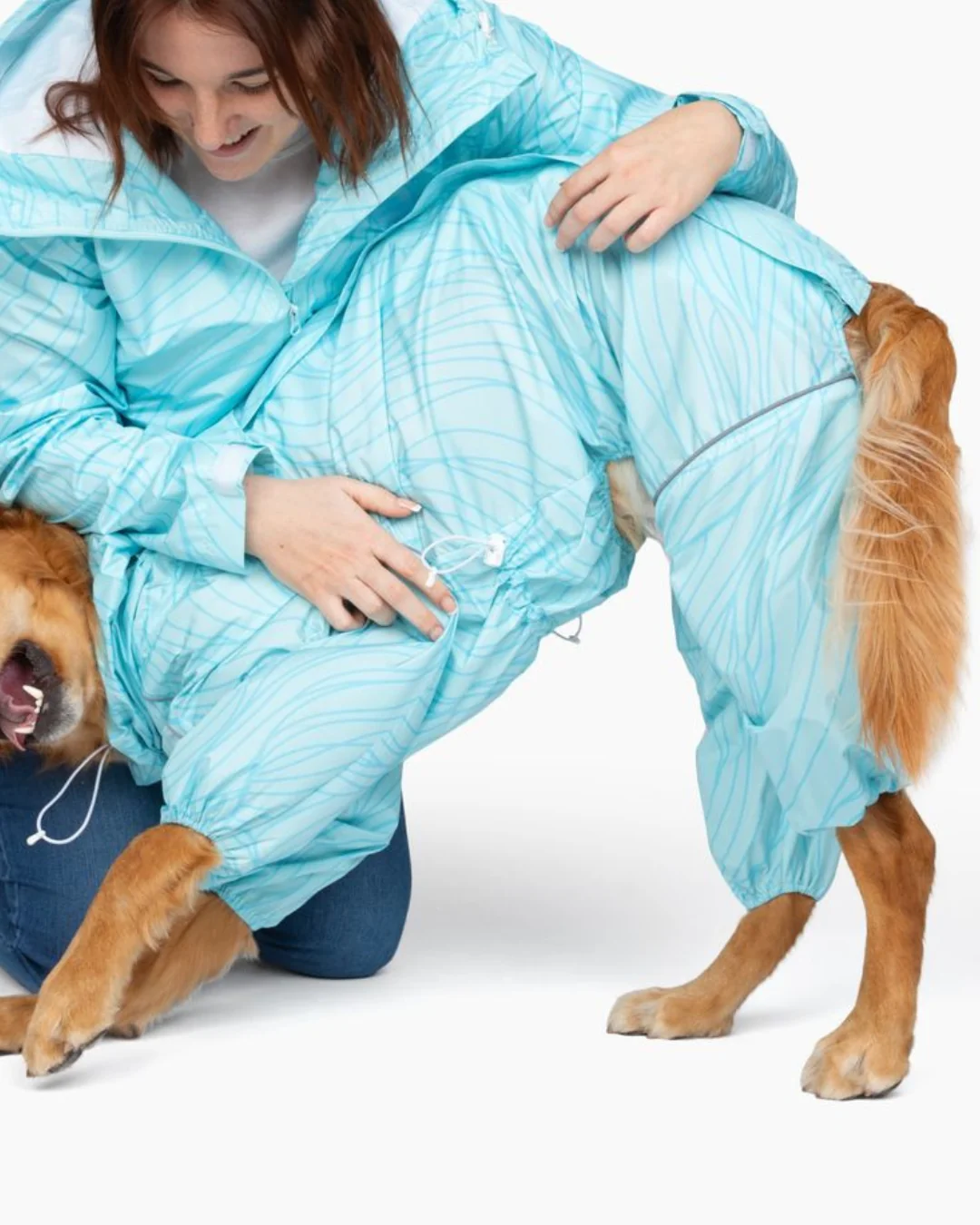 A woman and a dog wearing matching light blue, full-body rain suits against a white background.