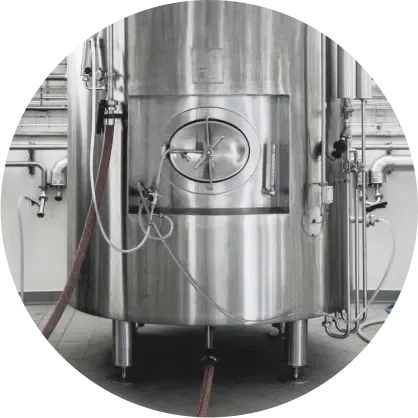 Large stainless steel industrial tank with pipes and valves in a factory setting.