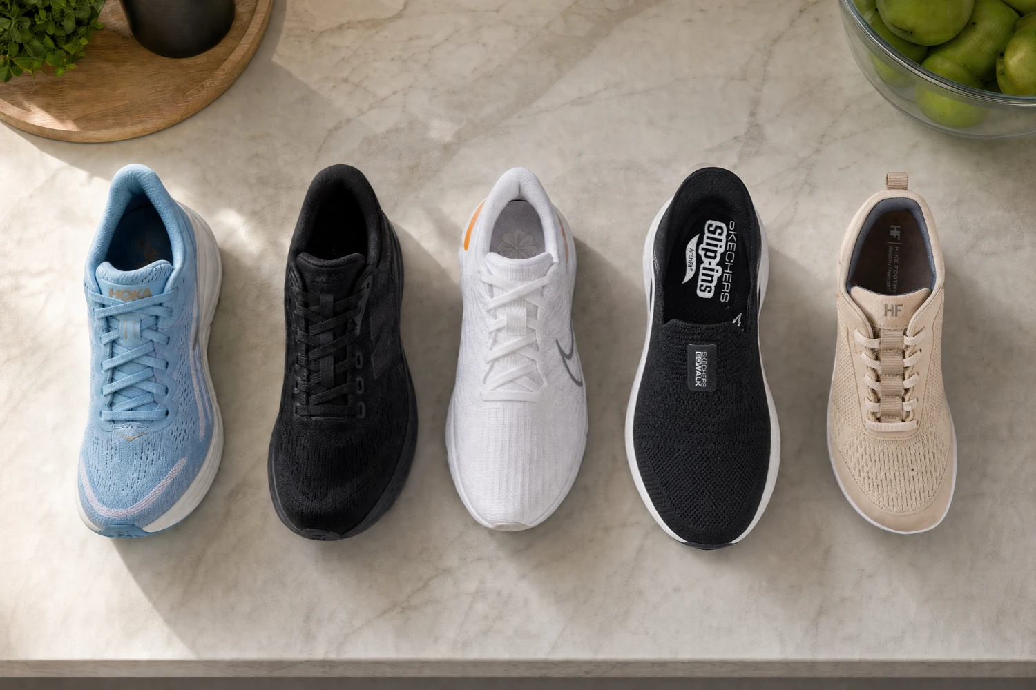 An overhead view of five different athletic shoes in various colors lined up on a marble surface.