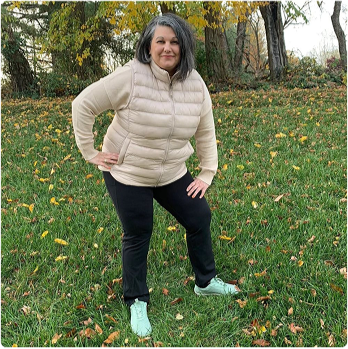 Person wearing a puffer jacket standing outdoors on grass with scattered autumn leaves.
