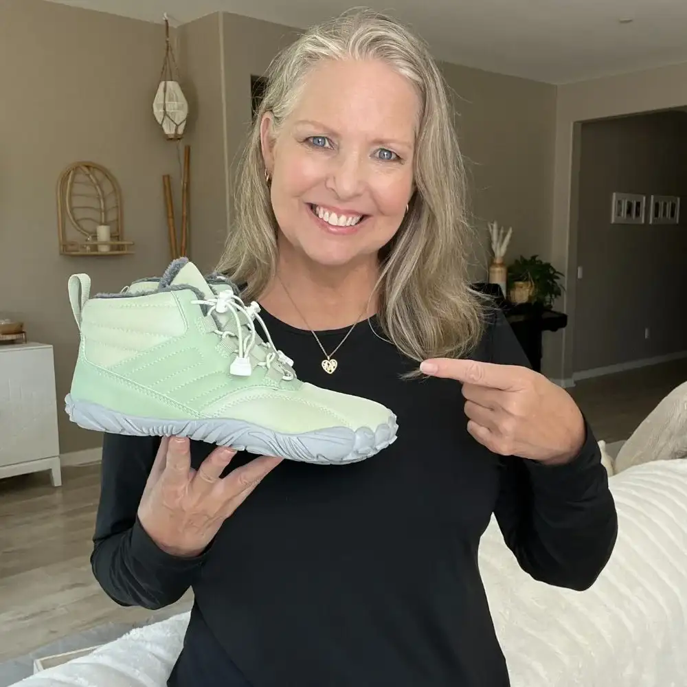 Woman smiling, holding a light green shoe, and pointing at it.