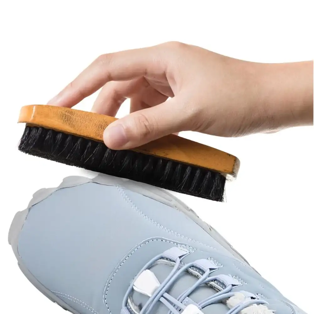 Hand cleaning a blue sneaker with a shoe brush.