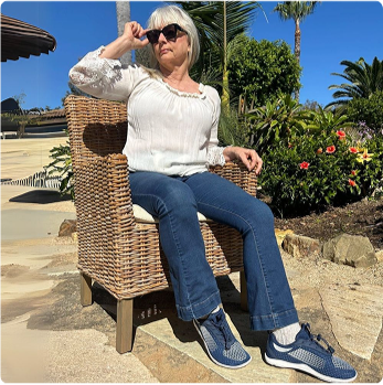 Person sitting in a wicker chair outdoors, wearing sunglasses and casual clothing.