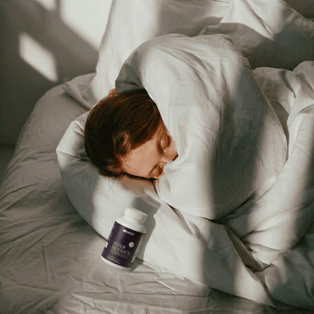 A person sleeps peacefully in a sunlit bed with a bottle of Sleep Sidekick supplements on the sheets.