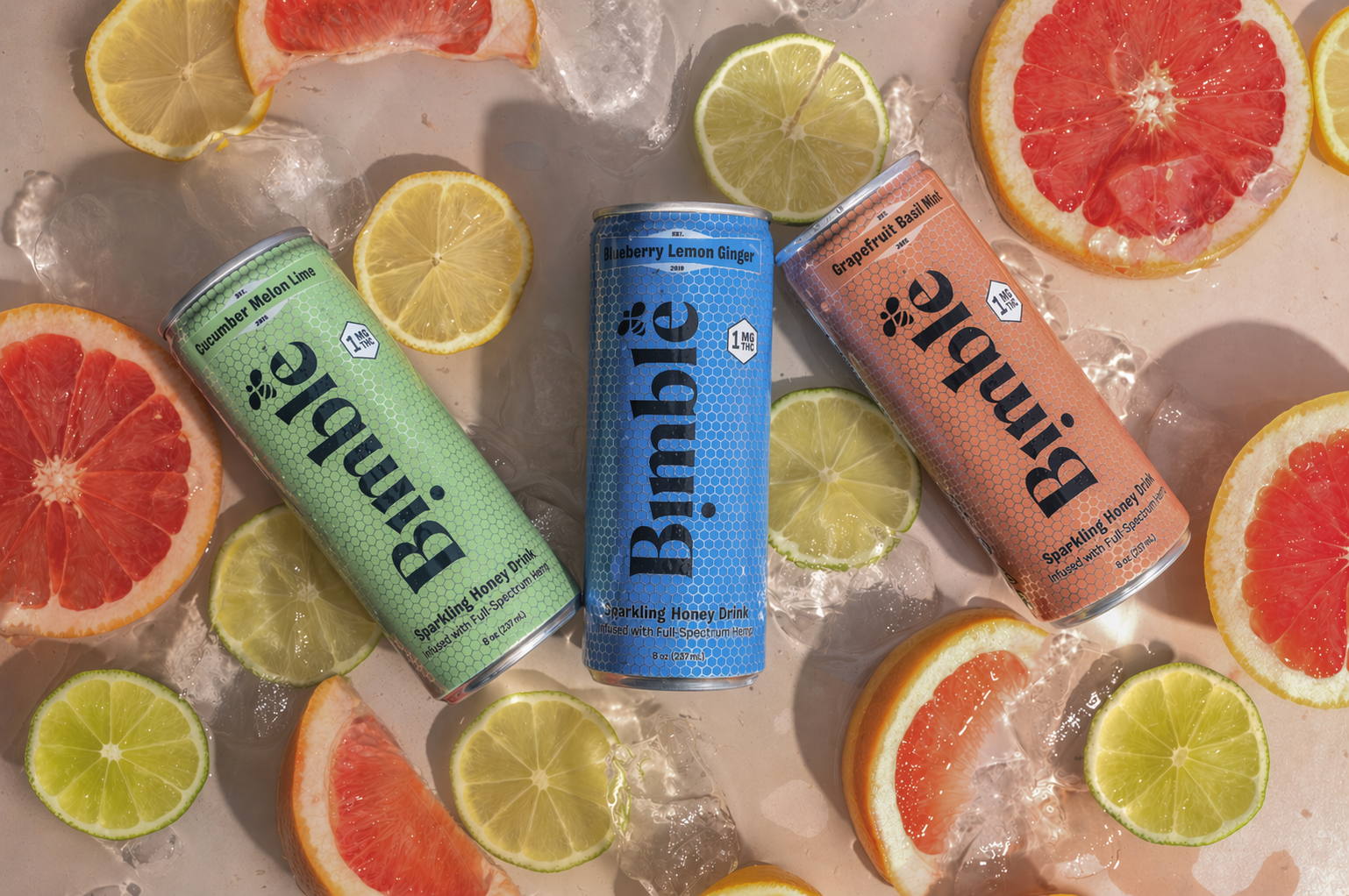 Three cans of Bimble sparkling honey drink laid on a surface with ice and slices of citrus fruit.