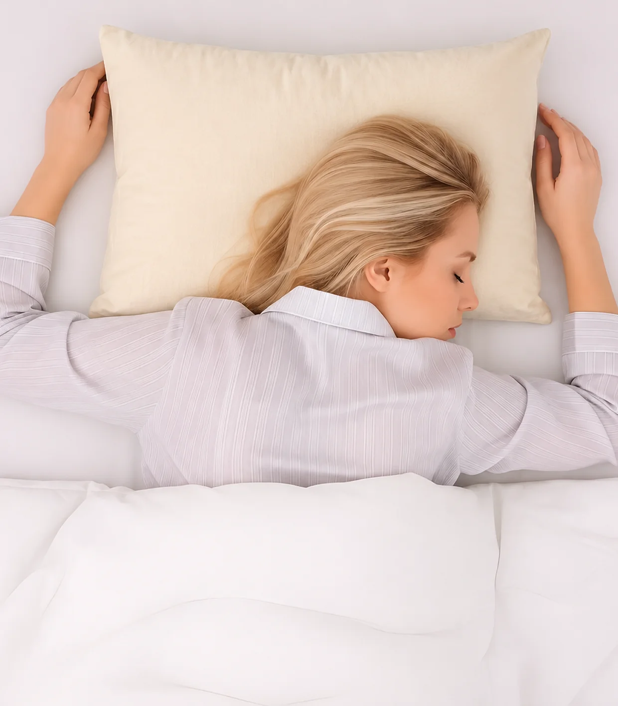 An overhead view of a blonde woman sleeping in bed on a cream-colored pillow.