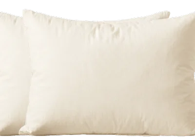 A close-up shot of two fluffy, cream-colored bed pillows against a white background.
