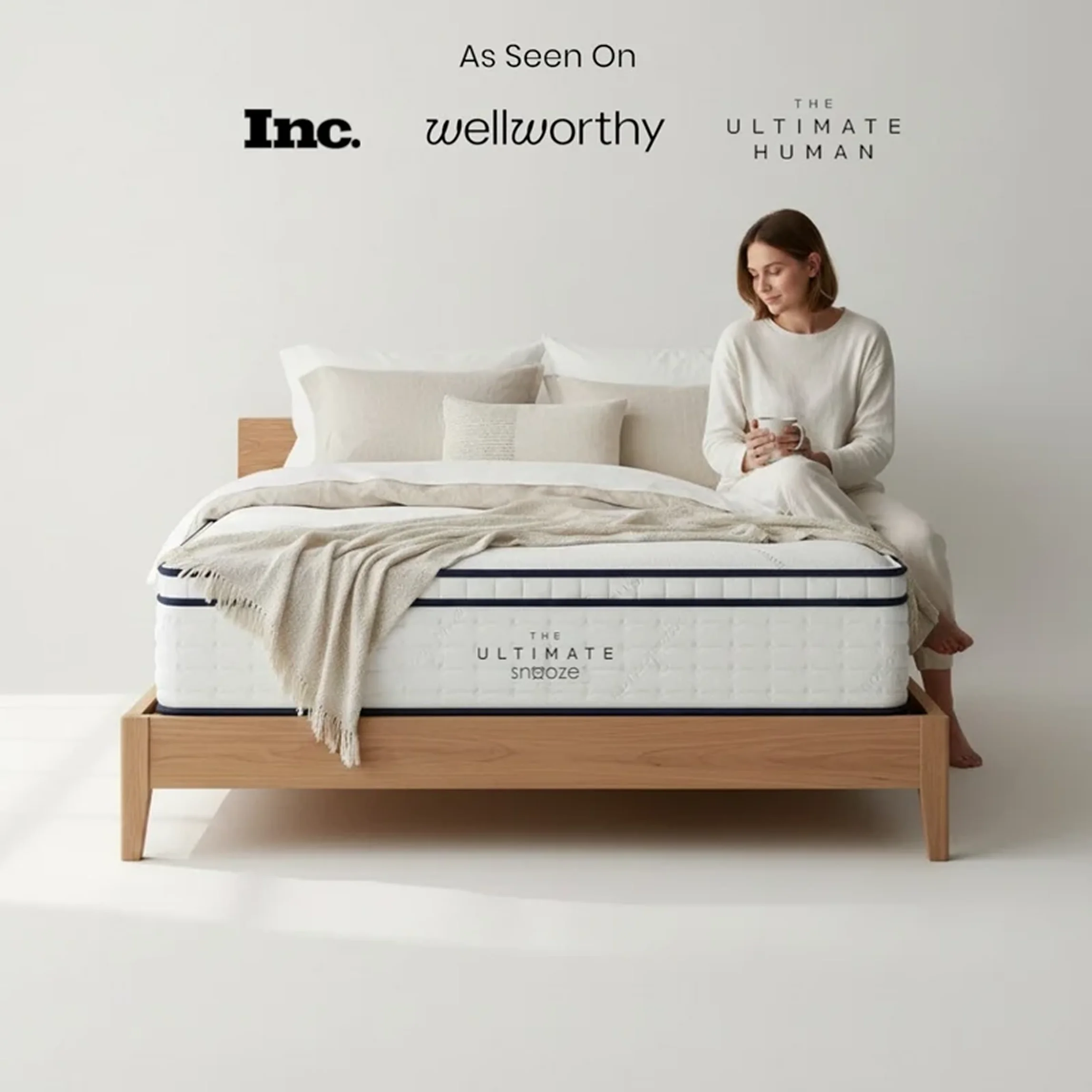 A woman in pajamas sits on the edge of The Ultimate Snooze mattress on a wooden frame.