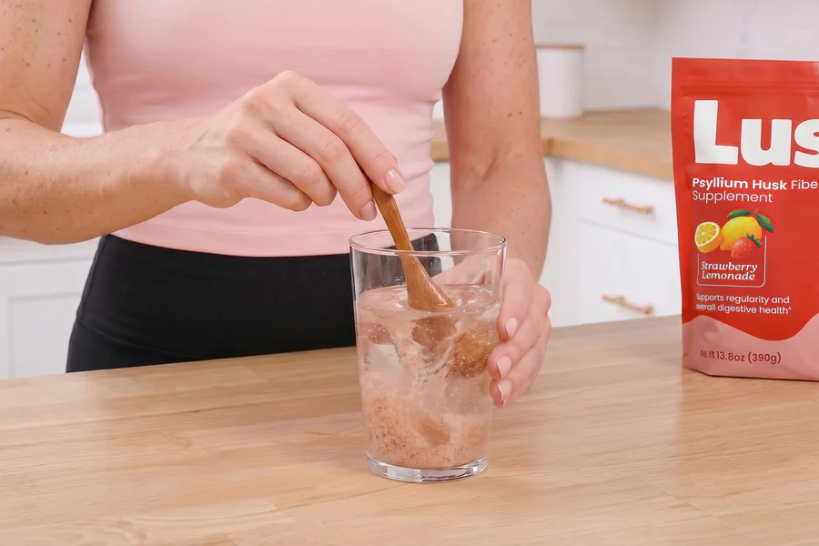 A person stirs a psyllium husk fiber supplement into a glass of water on a wooden counter.