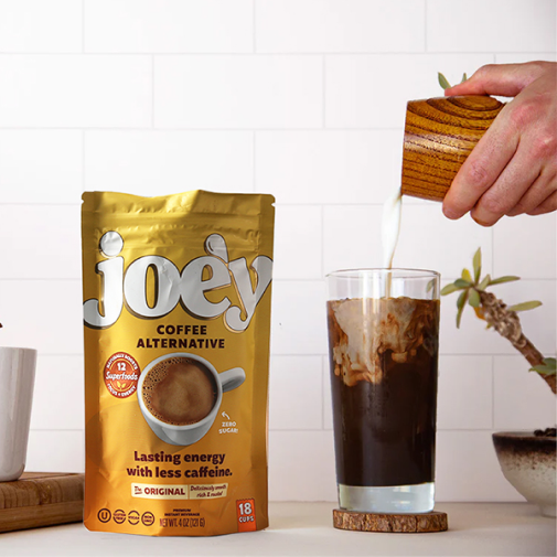 A hand pouring milk into iced coffee beside a Joey coffee alternative package.