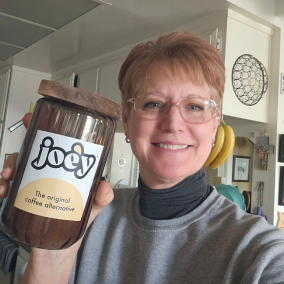 Person holding a jar labeled 'Joey, the original coffee alternative' in a kitchen.