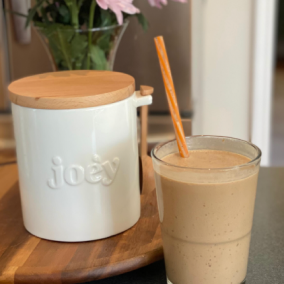 Glass of smoothie with straw next to a jar labeled 'joey' on a wooden tray.